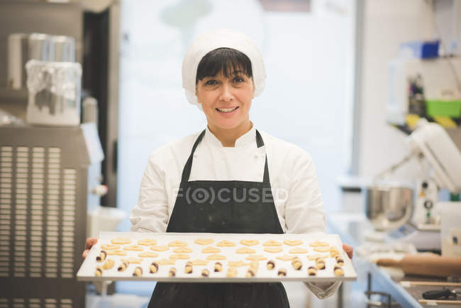 Bäckerin trägt Blech mit Gebäck in Küche — Stockfoto