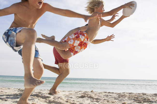 Boy and father running to reach brother with rugby ball on beach, Majorca, Spain — Stock Photo