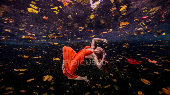 Woman wearing orange dress, floating towards water surface, underwater view — Stock Photo