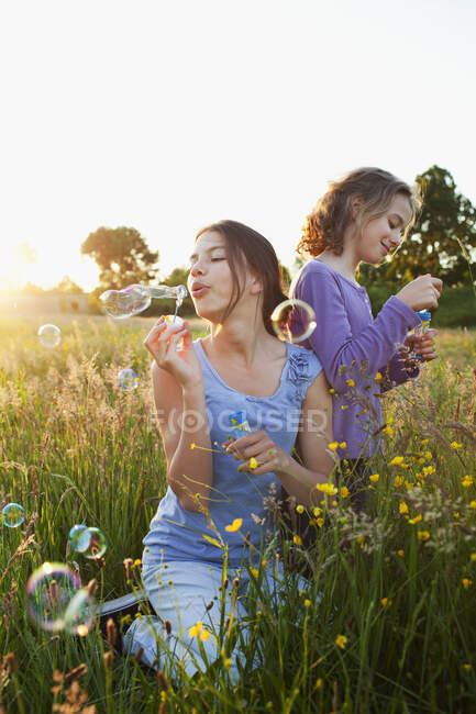 Sisters blowing bubbles in field — Stock Photo