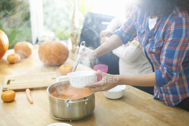 Madre sirviendo sopa de calabaza para hija en la cocina - foto de stock