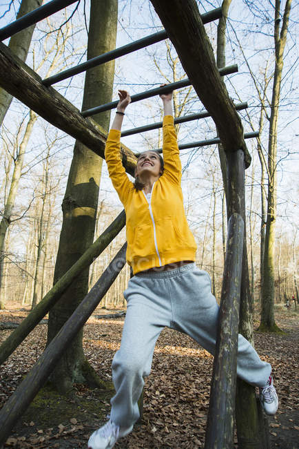 Young woman on climbing frame on assault course in forest — Stock Photo