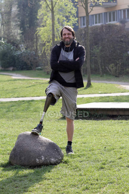 Porträt eines Mannes mit Beinprothese, der sich im Park an einen Felsen lehnt — Stockfoto