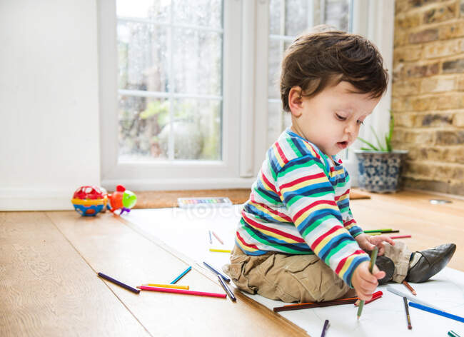 Criança do sexo masculino sentado no chão desenho em papel longo — Fotografia de Stock
