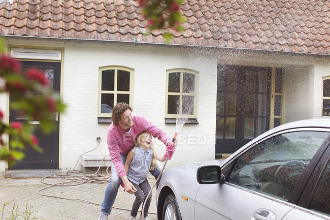 Fille aidant père lavage de voiture devant le bâtiment — Photo de stock