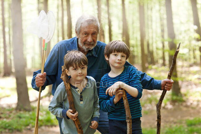 Grandfather and grandsons holding sticks in forest, portrait — Stock Photo
