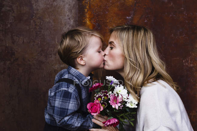 Молодий хлопчик дарує мамі купу квітів, мати цілує хлопчика — стокове фото