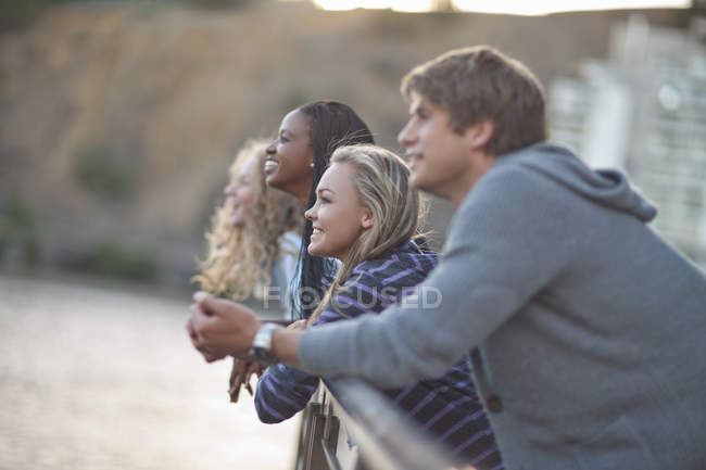 Vier junge erwachsene Freunde blicken von einem Geländer am Fluss — Stockfoto