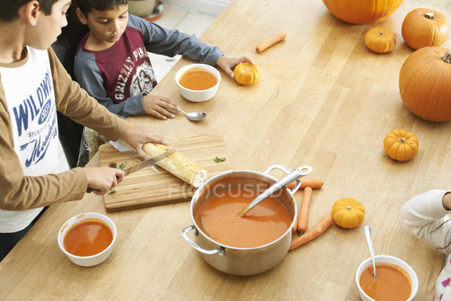 Fratelli e sorelle che preparano baguette e zuppa di zucca in cucina — Foto stock