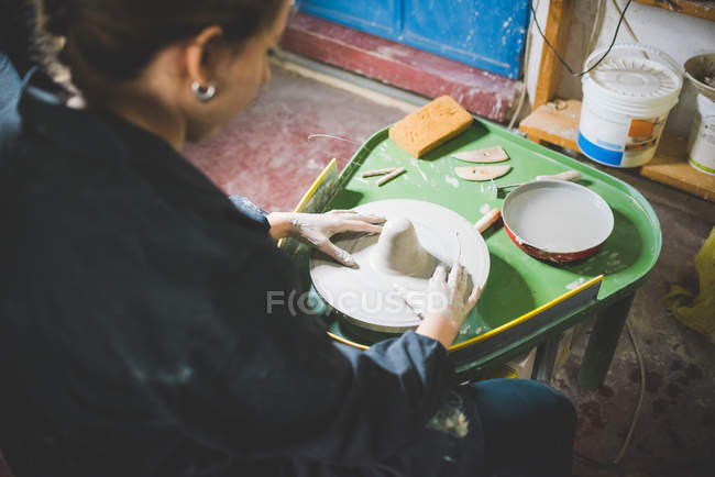 Vue sur l'épaule de la jeune femme assise en utilisant la roue de poterie — Photo de stock