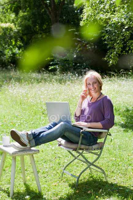 Усміхнена жінка використовує ноутбук на відкритому повітрі — стокове фото