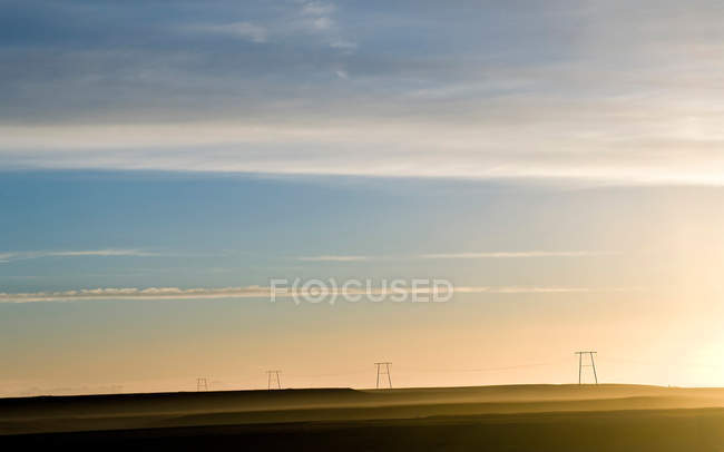 Champ vert avec pylônes et paysage nuageux au coucher du soleil — Photo de stock