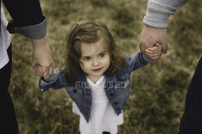 Мать и отец держат за руки молодую дочь, на открытом воздухе, возвышенный вид — стоковое фото