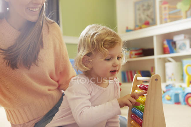 Mid adult woman and toddler daughter counting on abacus in playroom — Stock Photo