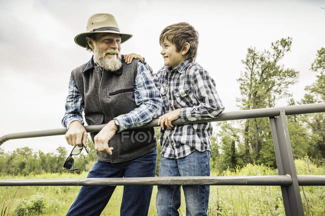 Бородатый мужчина и мальчик отдыхают на воротах улыбаясь — стоковое фото