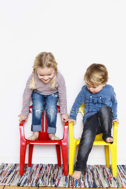 Menino e menina, agachado em cadeiras coloridas — Fotografia de Stock