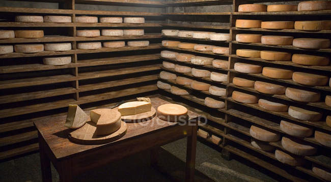 Ruote di formaggio su scaffali e tavolo — Foto stock