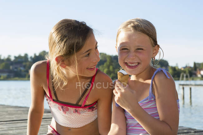 Two sisters on pier eating ice cream cones, Lake Seeoner See, Bavaria, Germany — Stock Photo