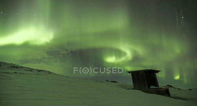 Luzes do norte no céu sobre a colina e a cabine cobertas de neve — Fotografia de Stock