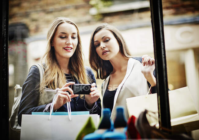 Молоді жінки купують вікна, фотографуючи зі смартфоном — стокове фото