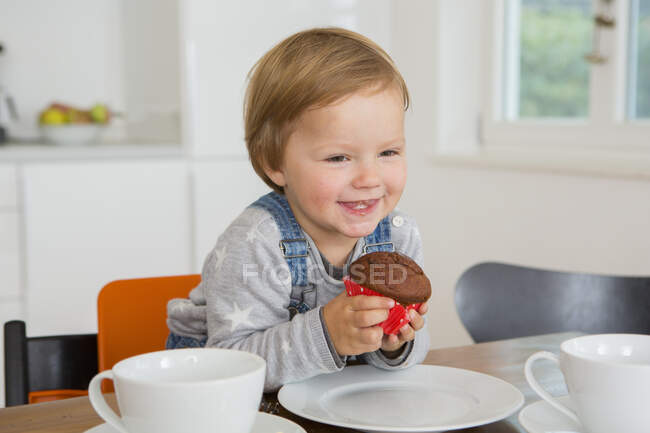Cute female toddler holding cupcake at kitchen table — Stock Photo