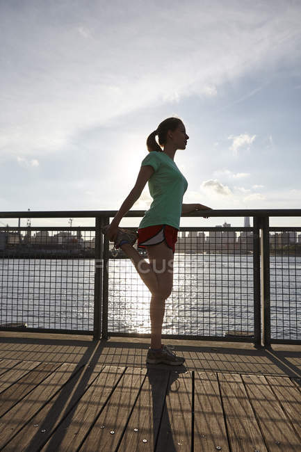 Side view of woman stretching leg on pier, Manhattan, New York, USA — Stock Photo