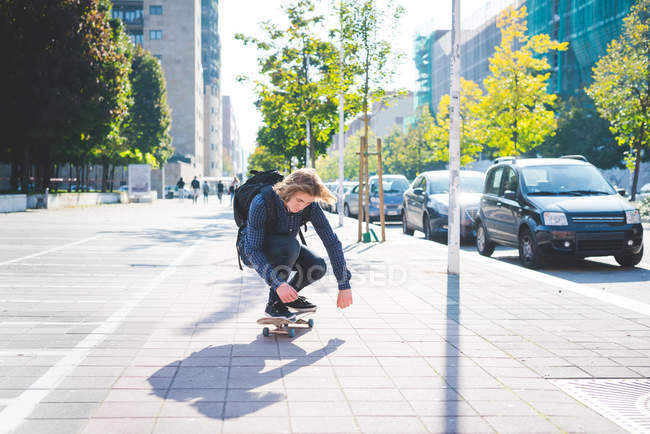 Jovem skatista do sexo masculino agachado enquanto skate na calçada — Fotografia de Stock