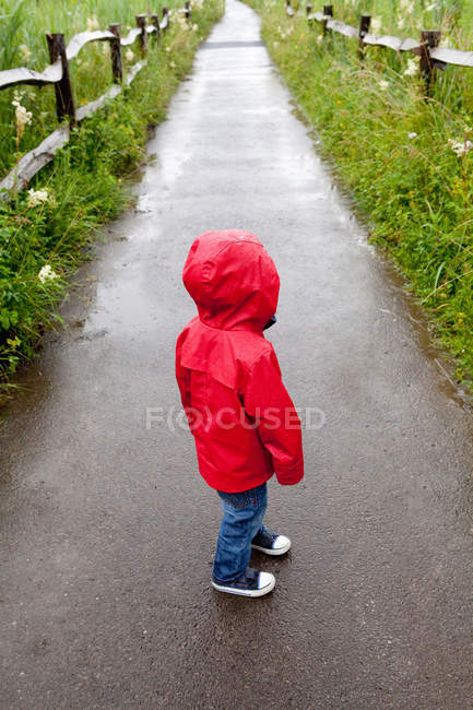 Rückansicht von Kleinkind, das in rotem Regenmantel auf Gehweg steht — Stockfoto