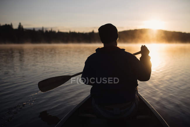 Старший чоловік катається на каное на озері на заході сонця, вид ззаду — стокове фото