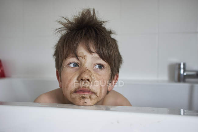 Boy with muddy face sitting in bath indoors — Stock Photo