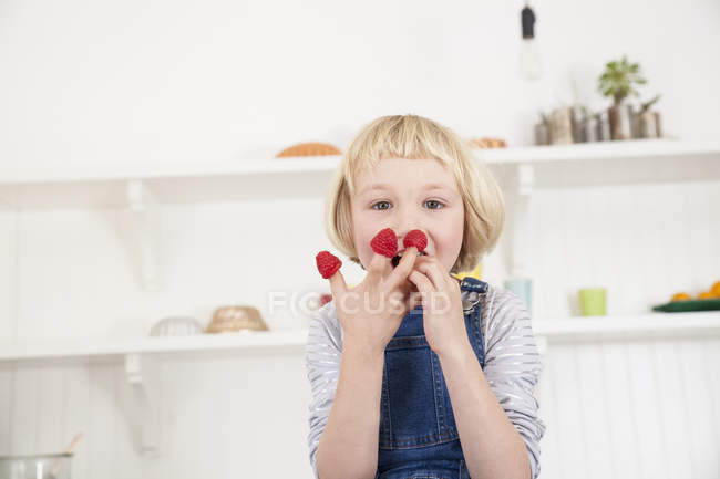 Portrait of cute girl with raspberries on her fingers in kitchen — Stock Photo