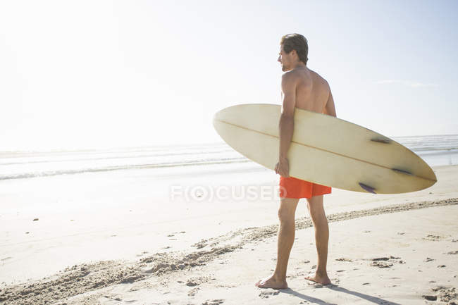 Young male surfer looking out to sea from beach, Cape Town (Ciudad del Cabo), Western Cape, Sudáfrica - foto de stock