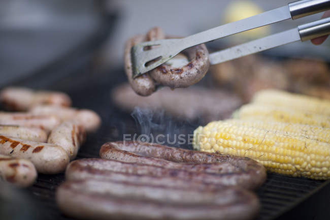 Barbecuant saucisses et maïs sur l'épi — Photo de stock