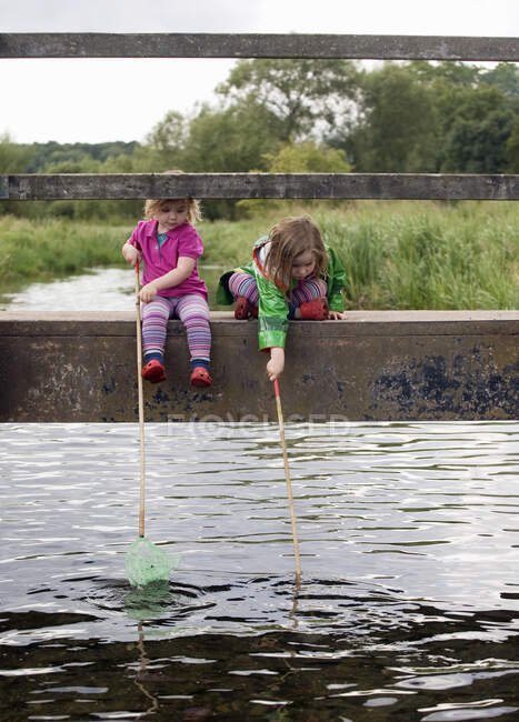 Two girls sitting on bridge with fishing nets, Amersham, Buckinghamshire, England, UK — Stock Photo