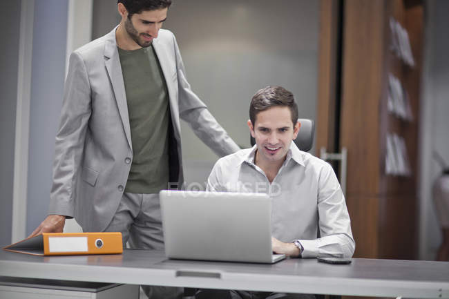 Два бизнесмена в офисе используют ноутбук и разговаривают — стоковое фото