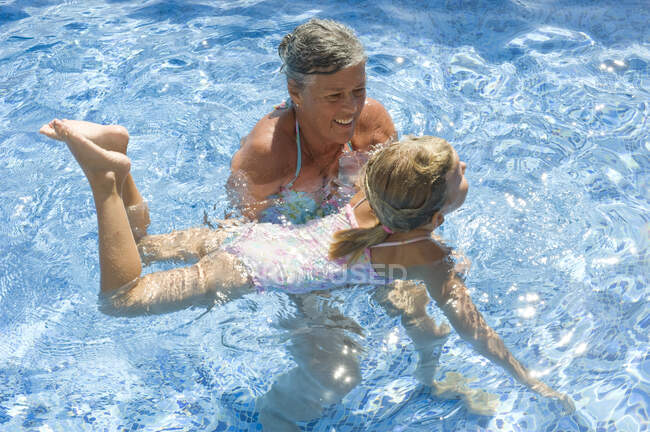Una mujer mayor enseñando a nadar a una chica - foto de stock