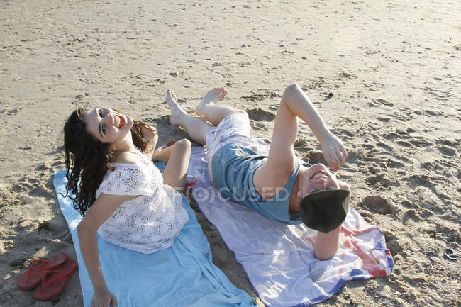 Portrait of young couple on towels on beach looking up — Stock Photo