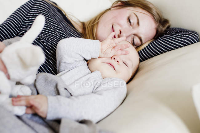 Tired baby girl and mother reclining on sofa — Stock Photo