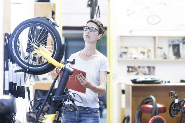 Woman in bicycle workshop holding clipboard checking bicycle — Stock Photo
