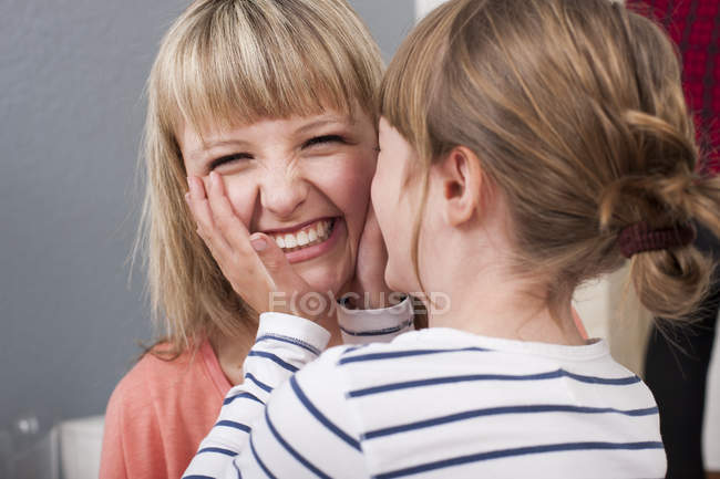 Menina pré-adolescente cupping em mãos rosto de rir jovem mulher — Fotografia de Stock