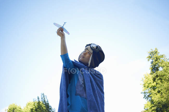 Jeune garçon en robe fantaisie, jouant avec un avion jouet — Photo de stock