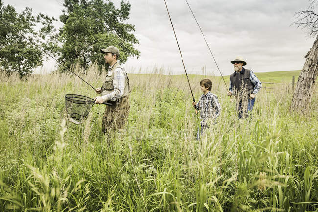 Familia multigeneracional en el campo que lleva cañas de pescar y red de pesca - foto de stock