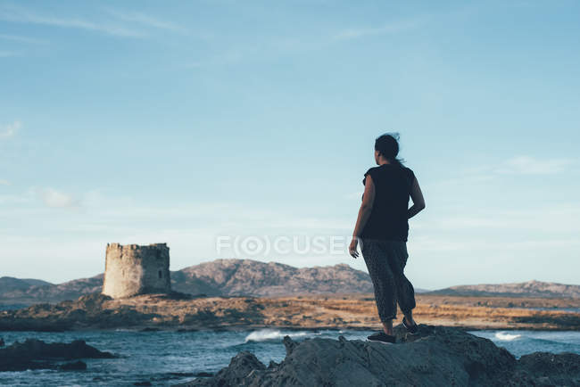Vue arrière de la femme sur des rochers regardant à travers la mer au phare abandonné, Stintino, Sassari, Italie — Photo de stock