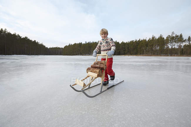 Мальчик толкает брёвна на кикле через замерзшее озеро, Гавле, Швеция — стоковое фото