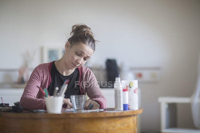 Femme mûre assise au bureau, écrivant — Photo de stock