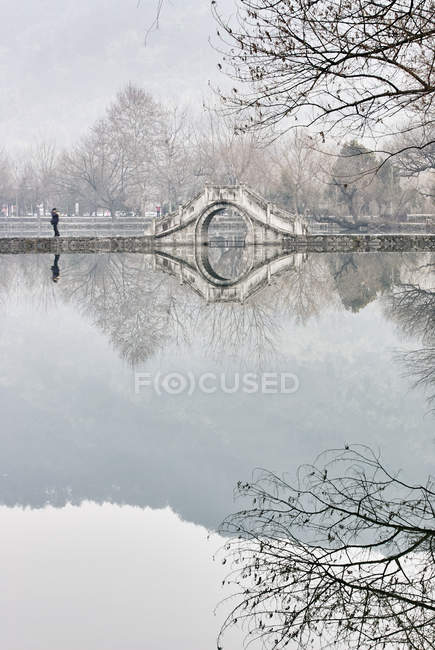 Mirror image of bare trees and footbridge over lake, Hongcun Village, Anhui Province, China — Stock Photo