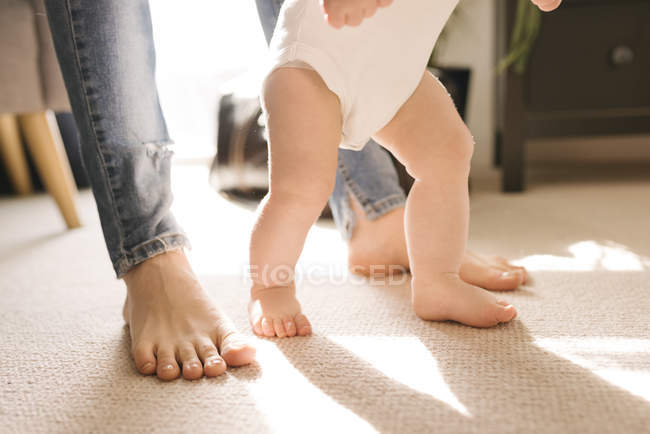 Mother and baby's bare feet on carpet in living room — Stock Photo
