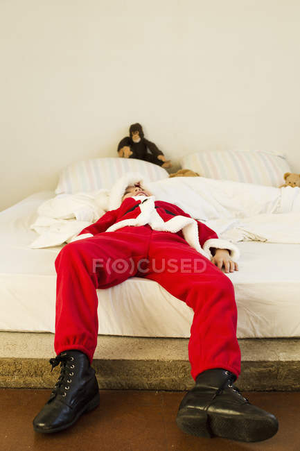 Menino vestido de Papai Noel deitado na cama — Fotografia de Stock
