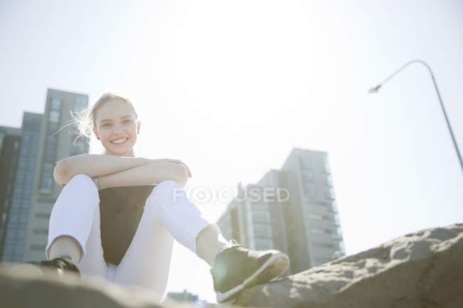 Low angle view of high rise buildings and teenage girl sitting on rocks looking at camera smiling, Reykjavik, Iceland — Stock Photo