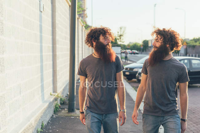 Identical male adult twins strolling and chatting on sidewalk — Stock Photo